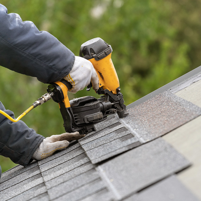 Workman using pneumatic nail gun install tile on roof of new house