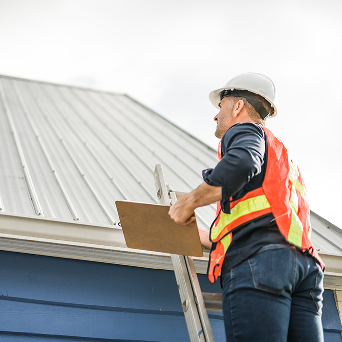 Worker with hard hat standing on steps inspecting house roof