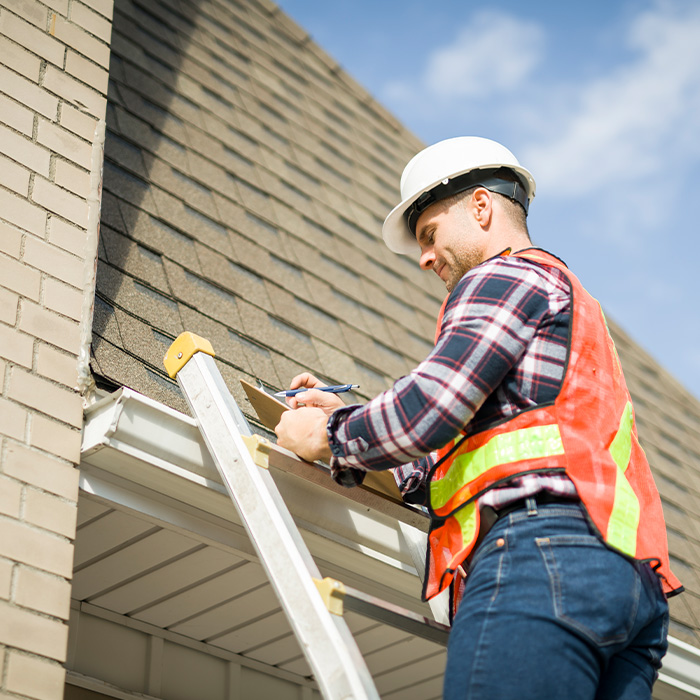 Man with hard hat standing on steps inspecting house roof