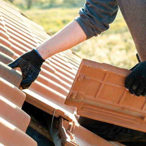 Worker hands installing yellow ceramic roofing tiles